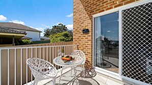 Un balcon avec une table et des chaises, une bouteille de vin et une assiette de nourriture.