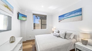 Une chambre avec un grand lit, une télévision et une fenêtre donnant sur la plage.