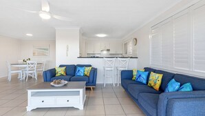 A modern living room with a blue sofa set, white dining table, and a coffee table. - Ocean Outlook 2 on Marine Parade (KINGSCLIFF)