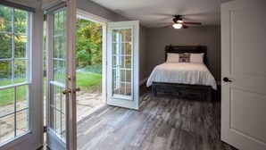 A bedroom with a bed, a ceiling fan, and a view of a garden through open French doors.