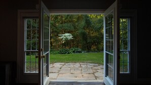A doorway leading to a stone patio with a view of a garden and trees.