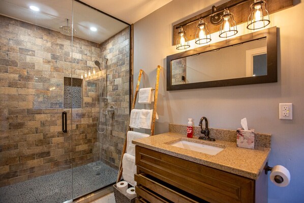 A bathroom with a glass-enclosed shower, a vanity with a mirror, and a towel rack.