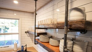 A kitchen with white tiled walls, wooden countertops, and shelves holding plates, bowls, and glasses.