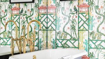 Une salle de bain avec une baignoire sur pieds noire, des robinets dorés et un papier peint à motifs représentant du bambou et des éléments d’architecture chinoise traditionnelle.