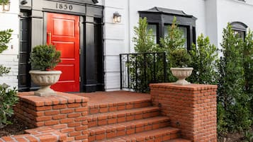 A white building with a red door, numbered 1850, and a brick staircase leading to the entrance.