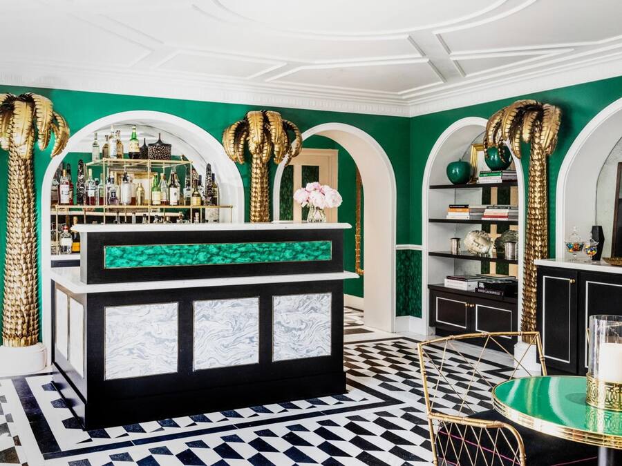 A bar area with a black and white checkered floor, a green and white marble counter, and golden palm tree decorations.