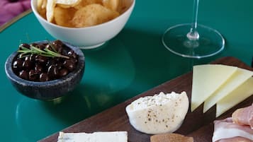 A charcuterie board with various cheeses, cured meats, olives, and crackers on a wooden board, accompanied by a glass of wine on a green table.