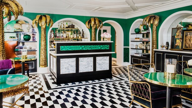 Zona de bar con piso de tablones, paredes verdes y detalles dorados.