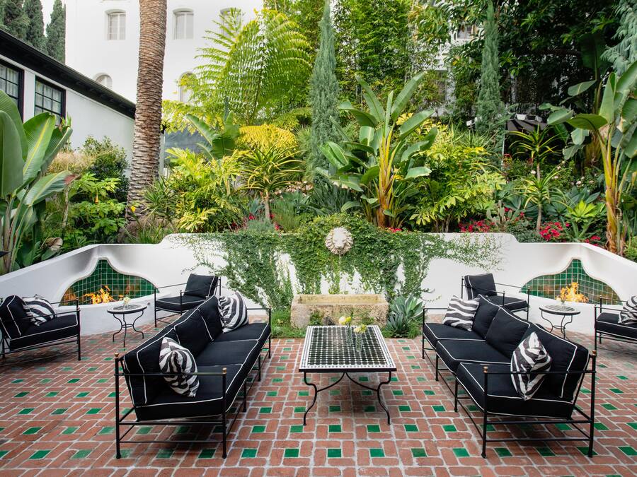 A patio with black outdoor furniture, a tiled floor, and a lush garden with various plants and a decorative wall.