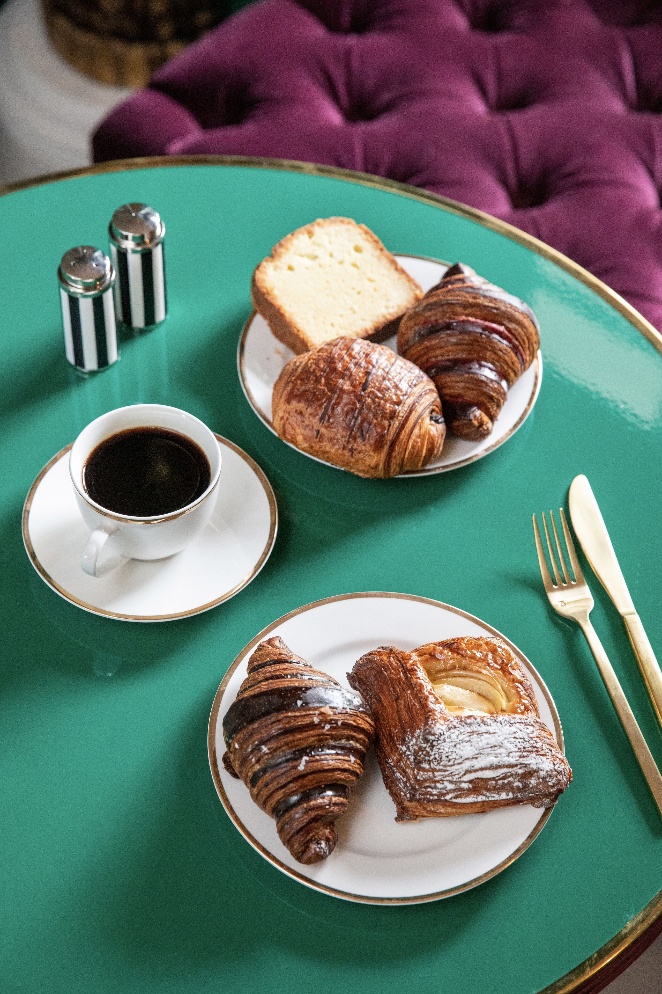 A table with a green tablecloth, two plates of pastries, a cup of coffee, and a fork and knife.