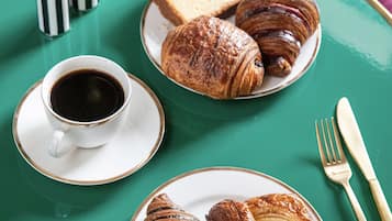 A table with a green tablecloth, two plates of pastries, a cup of coffee, and a fork and knife.