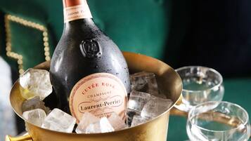 A bottle of champagne in a gold bucket with ice cubes, two empty glasses, and a green upholstered sofa in the background.
