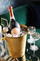 Une bouteille de champagne dans un seau doré rempli de glaçons, deux verres vides et, au fond, un canapé vert recouvert de tissu.