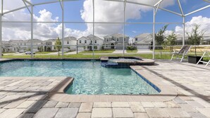 En swimmingpool med et overdækket område, stentfliser og udsigt til huse i baggrunden.