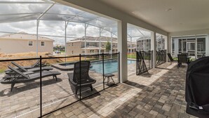 A covered outdoor area with a pool, lounge chairs, and a barbecue grill. - Champions Gate Resort!! Game room, theater, near Disney!!! (Davenport)