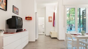 Una cocina moderna con zona de comedor, armarios blancos, un televisor y vistas amplias a través de grandes ventanales.