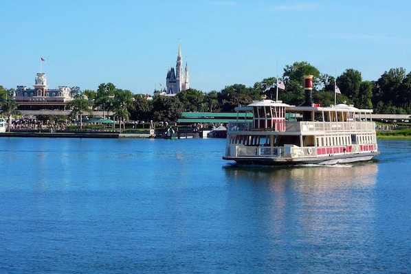 A riverboat with a white and red color scheme, docked near a large castle-like structure with spires.