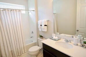 A modern bathroom with a bathtub, toilet, and sink. - 1816 Solara (Kissimmee)