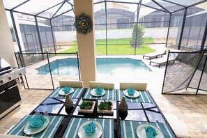 An outdoor dining area with a pool view, a grill, and a covered seating area. - 1816 Solara (Kissimmee)
