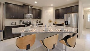 A modern kitchen with dark wood cabinets, stainless steel appliances, and a central island with bar stools. - 9009 Solara (Kissimmee)