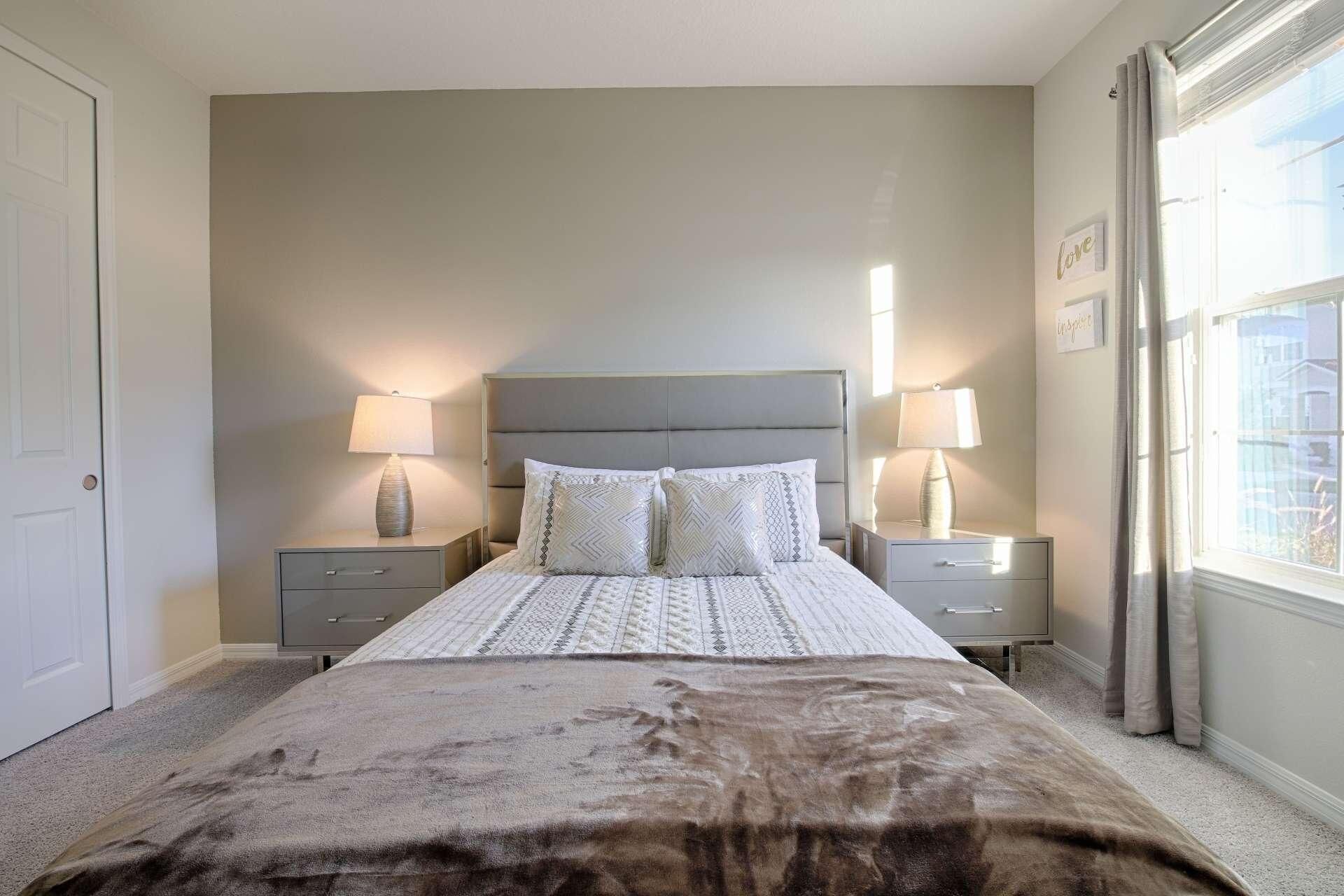 A bedroom with a large bed, two bedside tables with lamps, a window with curtains, and a door.
