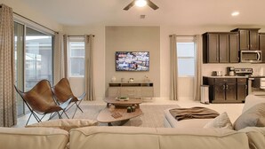 A living room with a sofa, a coffee table, and a TV mounted on the wall. - 9009 Solara (Kissimmee)