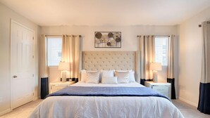 A bedroom with a large bed, two bedside tables, a headboard, and a decorative wall piece. - 9009 Solara (Kissimmee)