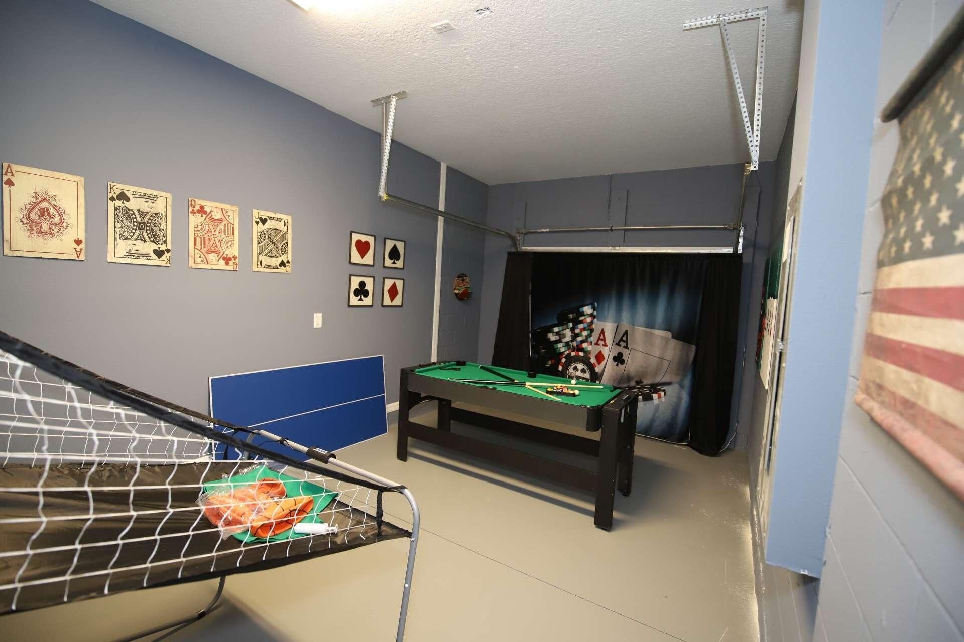 A room with a pool table, a ceiling-mounted rack, and a wall with framed playing cards.