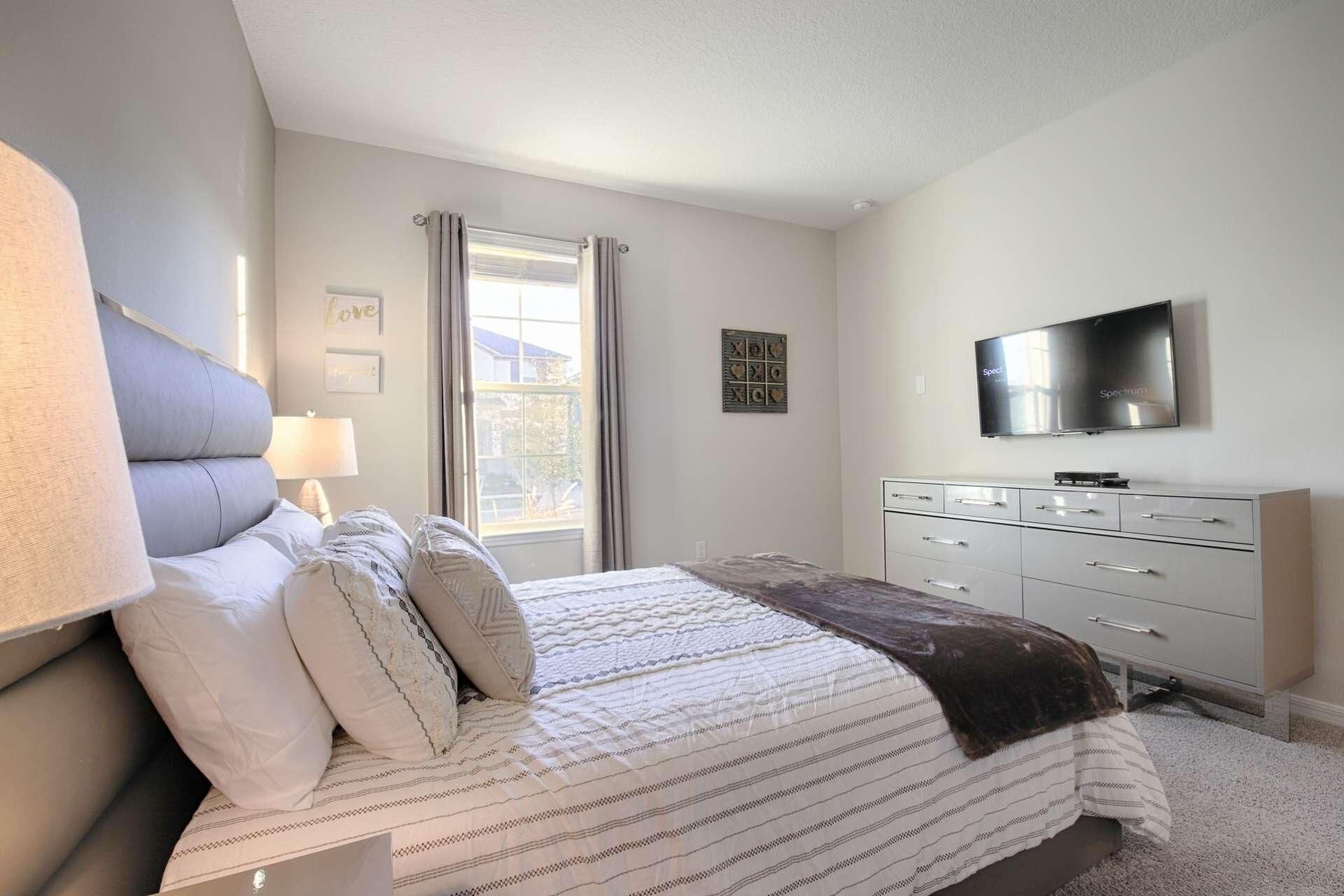 A bedroom with a bed, a dresser, a television, and a window with curtains.
