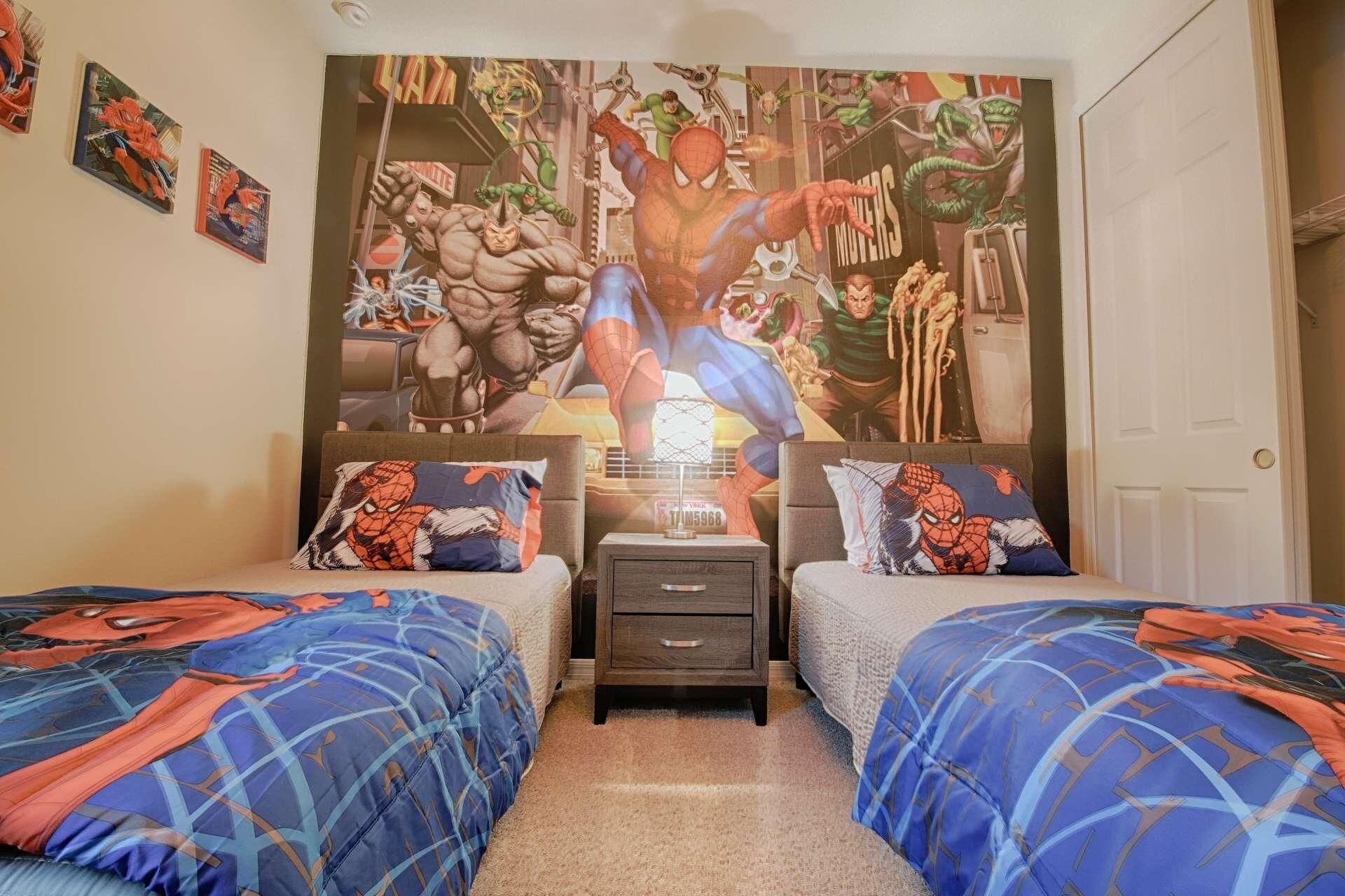 Une chambre avec deux lits, chacun recouvert d’une couette aux motifs de Spider-Man. Un grand décor mural représentant Spider-Man orne le mur derrière les lits.