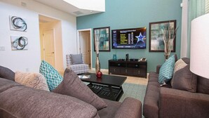 Een woonkamer met een flatscreen televisie, een bank, een salontafel en decoratieve kussens.
