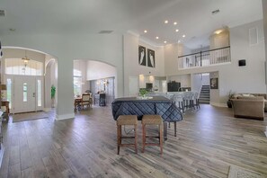 A spacious living area with a high ceiling, a dining area with a large table, and a kitchen in the background. - 625 Highlands Reserve (Davenport)