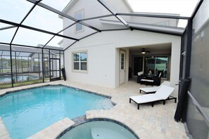 Een zwembad met een jacuzzi, omringd door een overdekt terras met ligbedden en een eethoek.