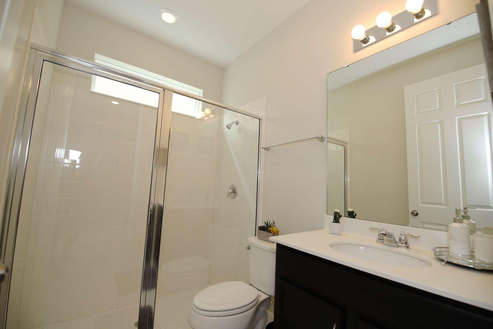 A bathroom with a glass-enclosed shower, a toilet, a sink with a mirror, and a vanity.