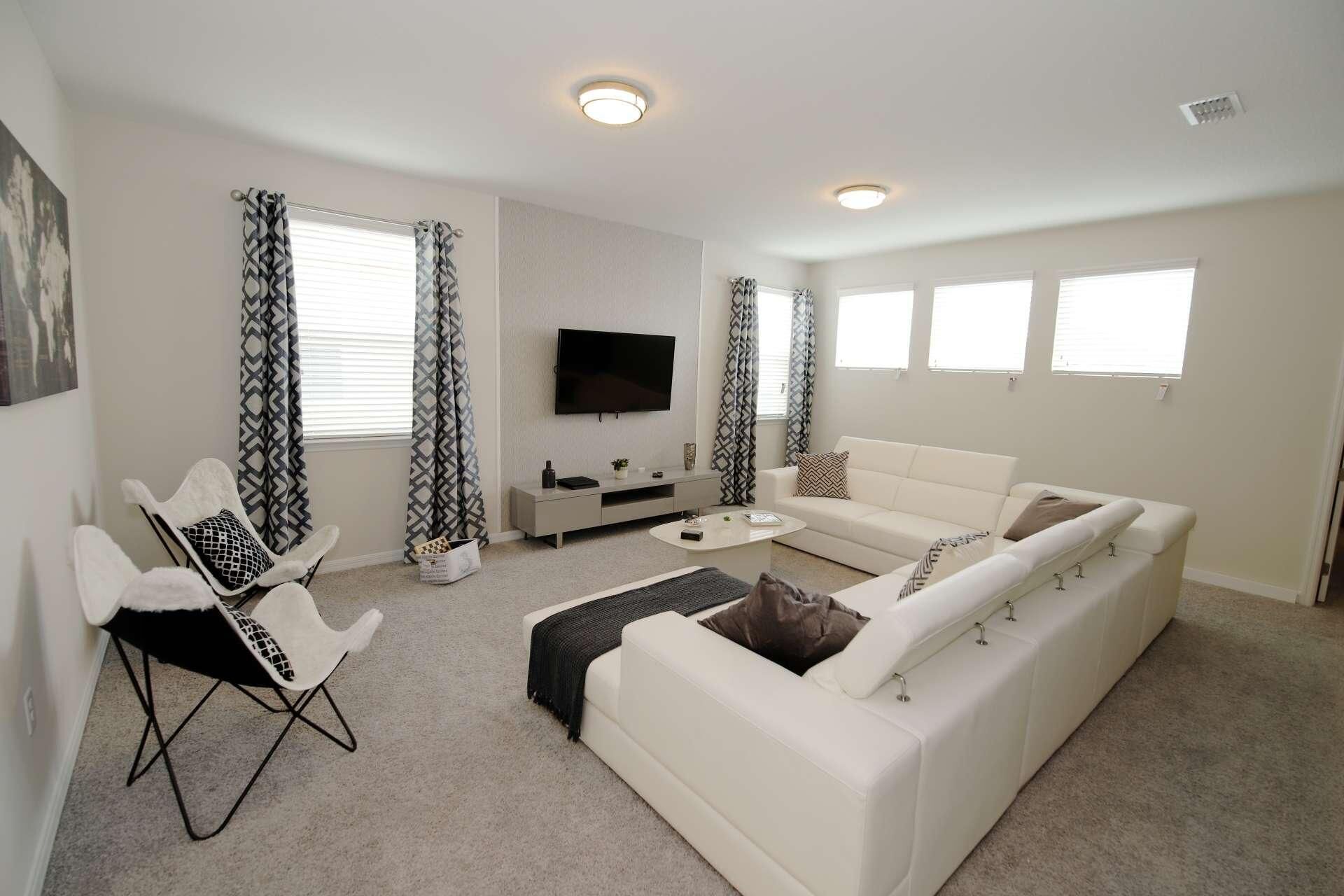 Een moderne woonkamer met een witte bank, een witte fauteuil, een salontafel en een tv die aan de muur is bevestigd.