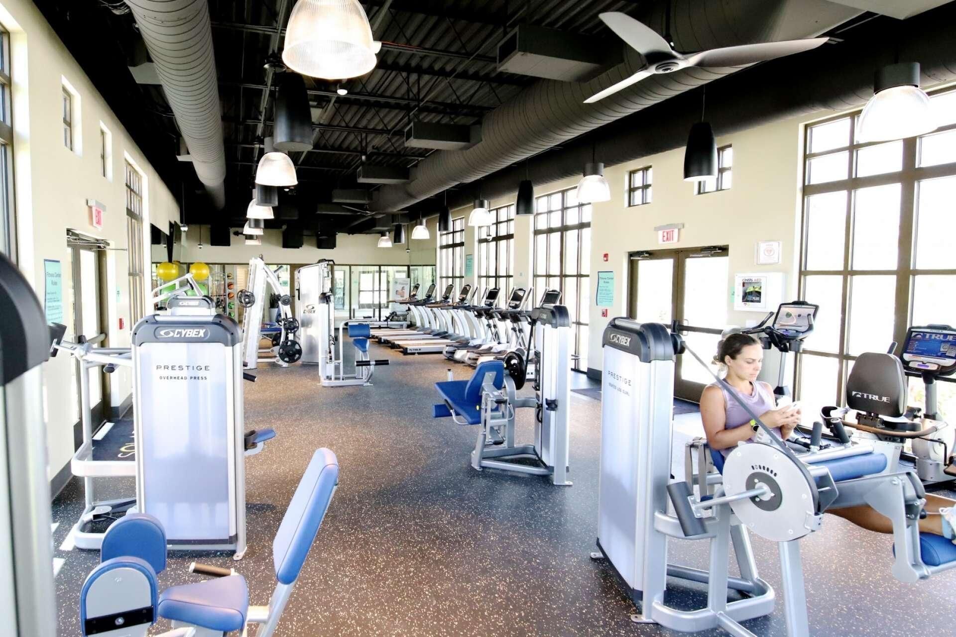 A gym with various exercise machines, including treadmills and weight stations, and a person using a stationary bike.