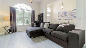 A modern living room with a sectional sofa, a TV, and a large window with curtains. - 600 Highlands Reserve (Davenport)