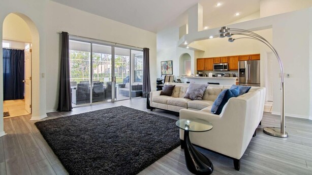 A spacious living area with a sofa, a glass door leading to a balcony, a modern kitchen, and a ceiling fan. - 600 Highlands Reserve (Davenport)