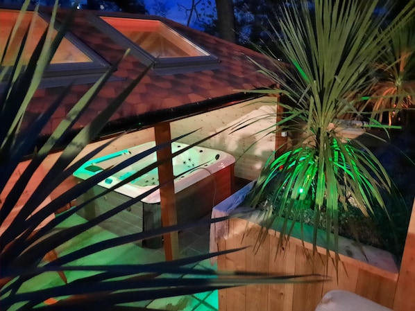 Un espacio de spa con estructura de madera, un jacuzzi y una planta de palma.