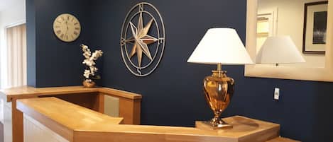 A reception desk with a clock, a compass wall decoration, and a lamp.