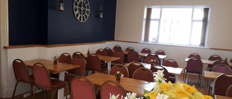 Un espace repas avec des tables et des chaises, une horloge murale et une fenêtre avec des rideaux.