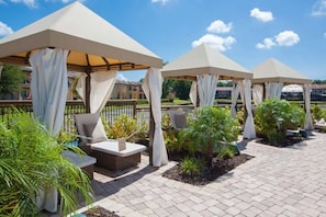 A series of outdoor seating areas with white canopies and cushioned chairs, surrounded by potted plants and a paved walkway.