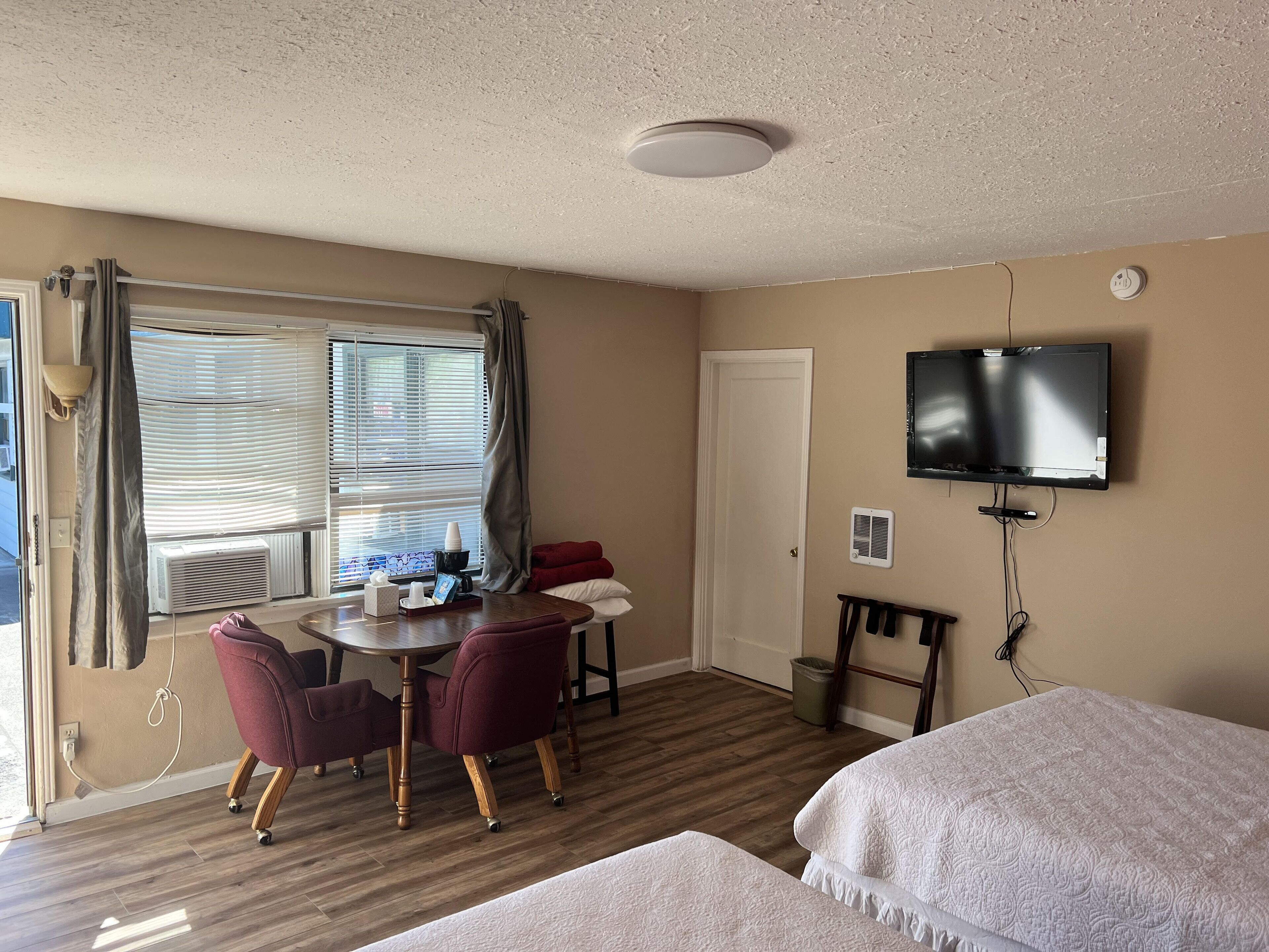 A hotel room with a dining table, chairs, a TV, a bed, and a window with curtains.