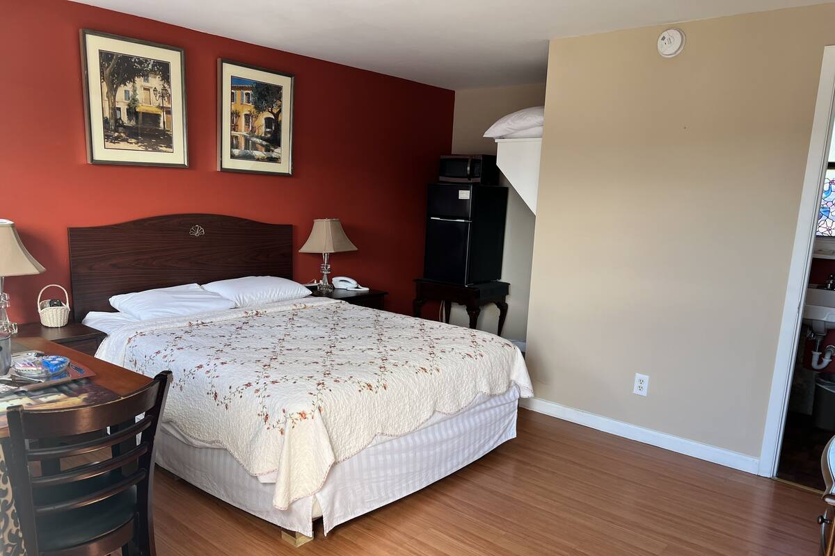 Quarto de hotel com cama, escrivaninha, luminária, telefone e micro-ondas.