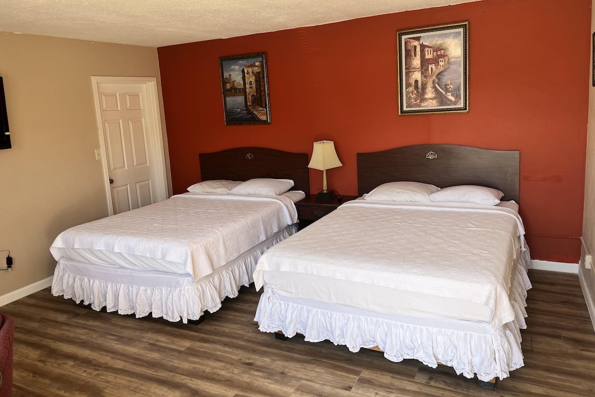 Quarto de hotel com duas camas, piso de madeira, uma porta branca e duas pinturas nas paredes.