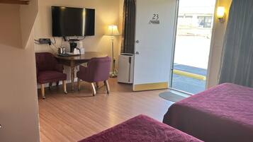 A hotel room with two beds, a desk with a chair, a television, a door with a 'No Smoking' sign, and a view of the outside.
