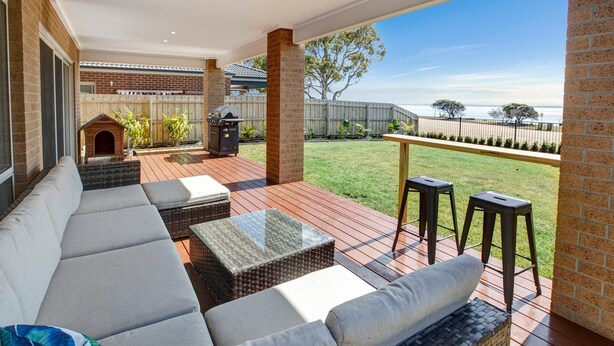 A covered outdoor seating area with a sofa, two tables, and a barbecue grill.