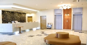 Una hall d'albergo con reception, area salotto e due ascensori.