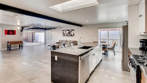 A modern kitchen with a central island, a dining area with a sofa and chairs, and a view through a glass door to an outdoor space.