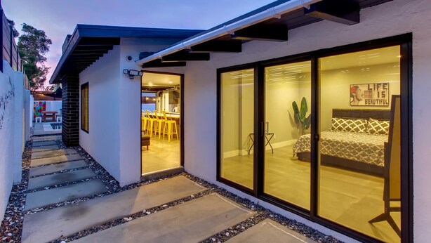 A modern house with a glass door leading to a dining area and a bedroom with a bed and a poster on the wall.
